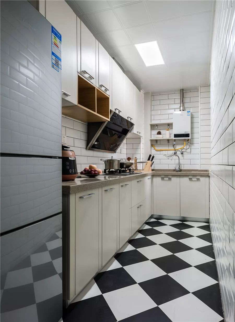 厨房是个狭长的空间，L型的橱柜布局让动线变得更为合理，黑白色菱形铺贴的地砖和小白砖的结合也让人感觉文艺而又时尚。